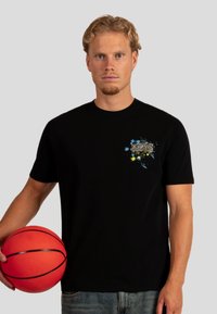 Zwart katoenen t-shirt met een kleurrafie op de linkerborst met de tekst "WRONG FRIENDS." Het model houdt een oranje basketbal vast.