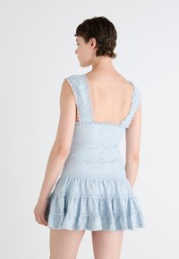 Svijetloplava čipkasta haljina s prilagođenim tijelom, volanima na rubu i širokim naramenicama obloženim čipkom. Sadrži cvjetne uzorke po cijelom materijalu.