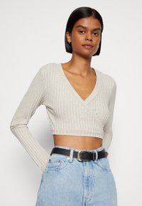 Suéter cropped creme canelado com decote em V e mangas longas, combinado com jeans azul claro de cintura alta e um cinto preto.