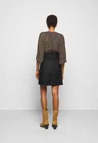 Svart knä-lång kjol i kombination med en mönstrad, flödande blus med trikå ärmar och tan-färgade klackboots.