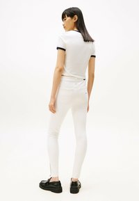 Vaqueros ajustados blancos de cintura alta, con diseño de bolsillo trasero y detalle de cremallera en el tobillo. Combinados con una camiseta blanca con detalles en azul marino.