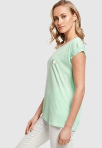 Minttivihreä lyhythihainen t-paita pyöreällä kaula-aukolla, jossa edessä pieni brodeerattu sydän- ja lehtimuotoilu. Sileä kangas rakenne.