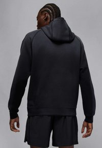 Czarna bluza z kapturem z fakturowanej tkaniny, z rękawami raglanowymi i kieszenią typu kangur. Połączona z czarnymi sportowymi szortami, minimalistyczny design.