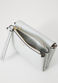 Sac à main en cuir gris clair avec une finition texturée, doté de deux compartiments zippés, d'accents noirs et d'une tirette en cuir.