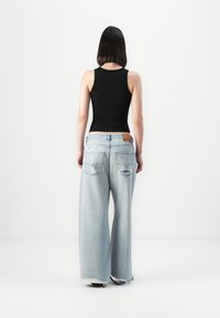 Jean large bleu clair avec des détails déchirés, associé à un débardeur noir ajusté. Comprend des poches et des ourlets effilochés.