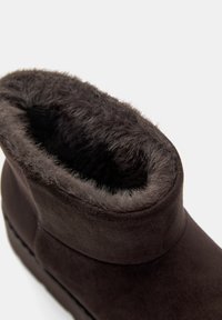 Stivale alla caviglia in suede marrone con morbido rivestimento in pelliccia sintetica, collo arrotondato e suola piatta. Presenta un esterno liscio con dettagli di cucitura discreti.