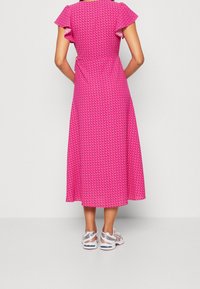 Lyserød midi-kjole med korte, flæsebesatte ærmer og et mønstret design. Båret med hvide og sølvfarvede sportssko. Glat stof, flydende silhuet.