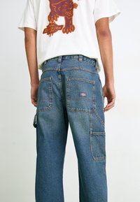 Modre denim cargo hlače z več žepi, sproščenim krojem in rahlo zbledelim videzom. Oblikovanje vključuje nalepko na zadnjem žepu.