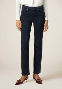 Marineblauwe, rechte broek met voorkruiszakken, een knoopsluiting en subtiele stikdetails. Gepaard met puntige hakken.