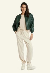 Veste en cuir vert, pull beige, joggers crème et baskets blanches. Textures douces, coupe décontractée et poignets élastiques sur la veste.