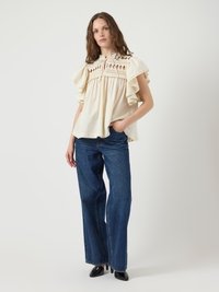 Ivory blouse with ruffled sleeves, featuring decorative smocking and open diamond patterns. Paired with wide-leg blue jeans and black heels.