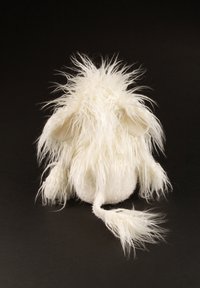 Fluffy white plush toy with long fur, rounded body, and small ears. Features a thin tail and textured accents. Background black.