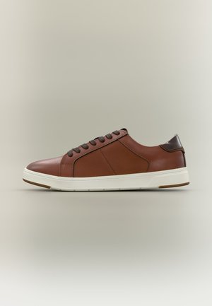 Baskets basses en cuir marron avec des lacets marron foncé, un panneau latéral texturé, une semelle blanche et une languette de talon marron foncé sur un fond neutre.