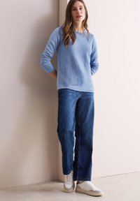 Lichtblauwe langemouwen trui met een relaxte pasvorm, gecombineerd met donkerblauwe rechte jeans en witte sneakers met grijze accenten.