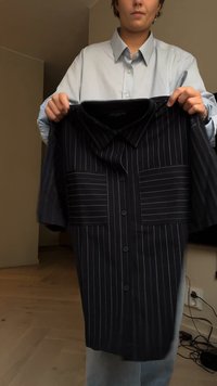 Camisa preta com riscas brancas verticais, mangas curtas, dois bolsos frontais e fecho por botões. Tecido macio, design com gola.