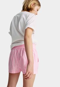 Rosa shorts met verticale witte strepen, elastische tailleband en een casual pasvorm. Gecombineerd met een wit T-shirt met korte mouwen.