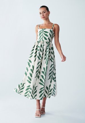 Maxi dress in cream fabric adorned with green leaf patterns, featuring a square neckline, thin straps, and a gathered waist.
