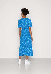 Blå midi-klänning med korta ärmar, prydd med ett vitt blommönster och knytbar midja. Bärs med vita höga sneakers.