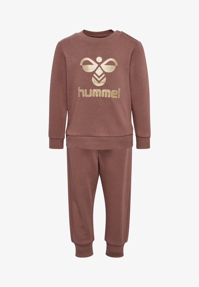 Tvådelat plagg i mjukt, brunt material. Består av en långärmad topp med en gyllene logotyp och matchande byxor med ribbade muddar. Enkelt design.