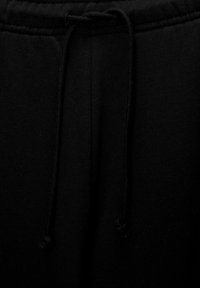Un pantalon de jogging noir avec une taille à cordon de serrage, une texture de tissu douce et deux poches latérales, affichant un design minimaliste.
