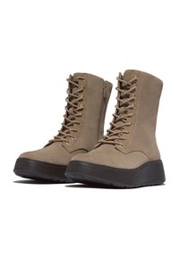 Enkellaarsjes van cognac suède met een dikke zwarte zool, gouden veteroogjes en veters; voorzien van een zijrits voor gemakkelijk aan- en uittrekken.