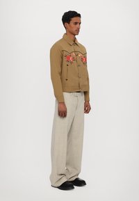 Taná košile s výšivkou květin, černými švy; spárováno s světle šedými kalhotami s širokými nohavicemi a černou obuví.