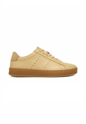 Sneaker beige in pelle basse con lacci abbinati, dettagli cuciti, cinturino in camoscio sul tallone e suola in gomma marrone, mostrata di profilo.