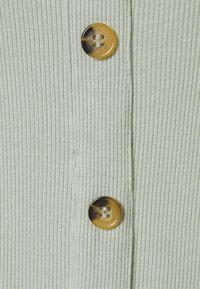 Žebrovaná světle zelená látka s vertikální texturou, opatřená dvěma lesklými hnědými knoflíky podél středu, které přidávají funkční prvek.