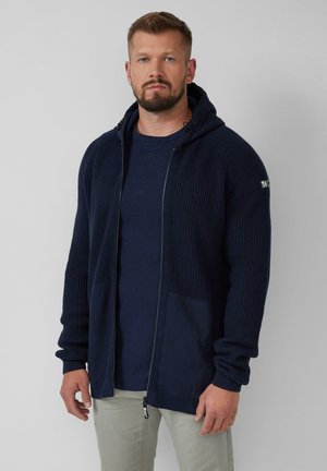 Navy ribbed knit zip-up hoodie with two front pockets, contrasting solid fabric accents, and a drawstring hood, layered over a navy T-shirt.