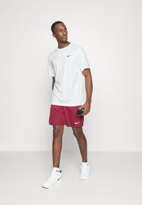 Men's athletic outfit featuring a light gray short-sleeve shirt and maroon shorts, both with Nike logos. Shoes are white sneakers.