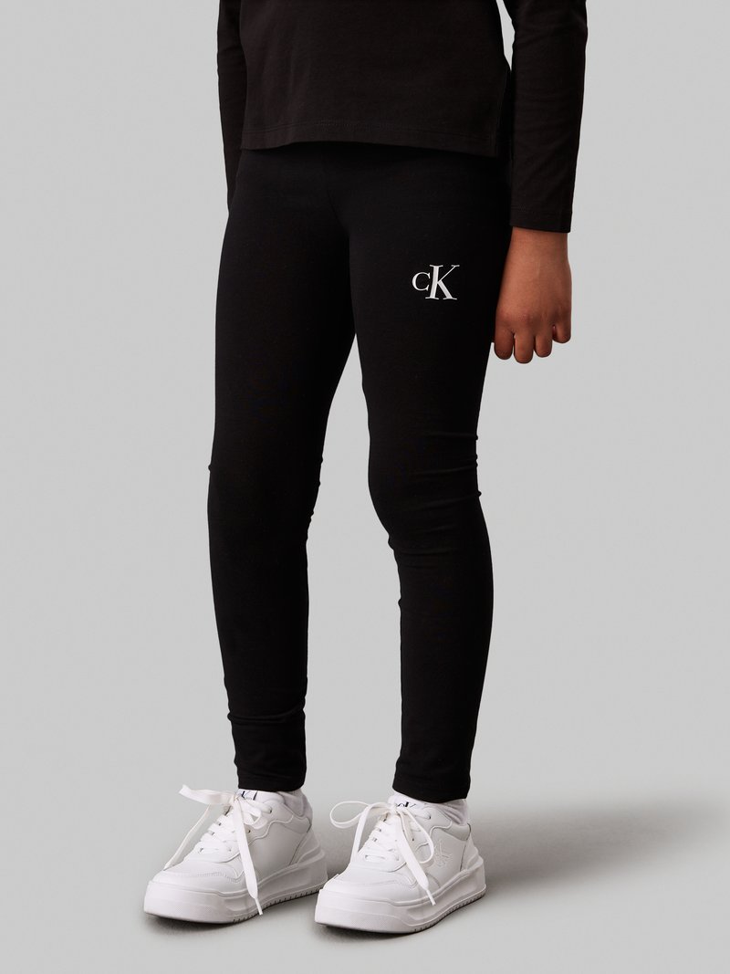 Svarta leggings gjorda av stretchy tyg med en åtsittande passform. Har en vit broderad "cK"-logotyp på låret. Matchas med vita sneakers.