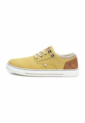 Zapatillas de lona en color mostaza con acentos en beige, suela de goma blanca y talón de cuero marrón. Presentan cordones redondos y costuras en contraste.