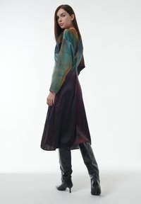 Lang, veelkleurige jurk met een gradient patroon in groene, oranje en zwarte tinten. Draag met hoge zwarte hakken. Stijlvolle textuur.