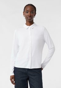 Camicia bianca a maniche lunghe con colletto, realizzata in tessuto morbido. Presenta una chiusura frontale completamente abbottonata e una vestibilità rilassata.