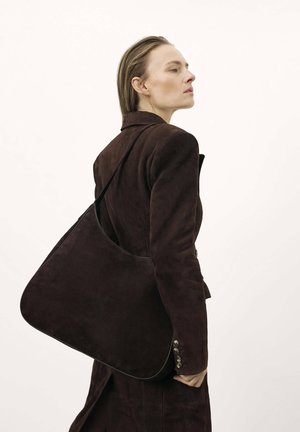 Bolso de hombro de ante marrón con forma curva, textura lisa y una única correa para el hombro, que presenta elementos de diseño minimalistas.