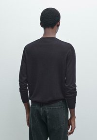 Pull à manches longues foncé avec un col rond, fabriqué dans un matériau lisse, associé à un jean noir délavé, présentant un design simple et ajusté.