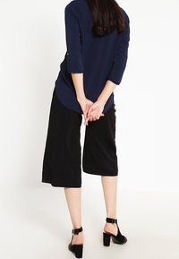 Marinblå långärmad topp med rundad nederkant, kombinerad med svarta vida culottbyxor och svarta klacksandaler med ankelrem.