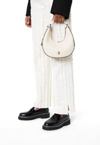 Biała torba typu hobo z czarną lamówką, złotymi elementami metalowymi i zamkiem błyskawicznym. Białe teksturowane spodnie z falbankami oraz czarne buty na platformie.