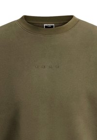 Olivgrüner Rundhalsausschnitt-Pullover mit dezent geprägtem "CORE"-Text auf der Brust und einem Jack & Jones Core-Label im Kragen.