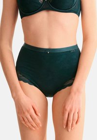 Culottes en dentelle verte taille haute avec une ceinture lisse, ornées de motifs floraux et de bords festonnés. Accent en métal argenté à l'avant.