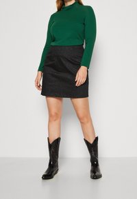 Un turtleneck vert à manches longues associé à une mini-jupe noire pailletée et des bottes de cowboy noires avec des détails en relief.