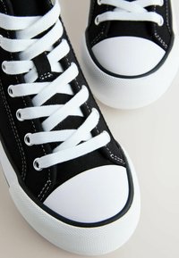 Mustad lõuendist tossud, millel on valged paelad, valge kummist varbakate ja tekstuuriga must tald nähtavate õmblusdetailidega.