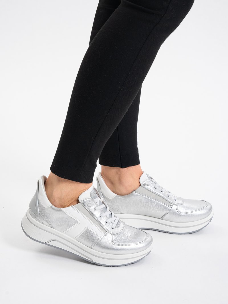 Person wearing silver metallic platform sneakers with white soles and white accents, paired with black fitted pants on a white background.