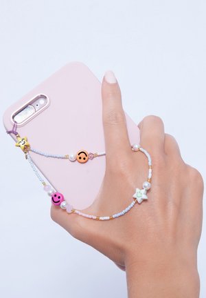 Coque de téléphone rose tenue dans une main, attachée à une bandoulière en perles avec des charms sourires et étoiles, des perles, et des perles de couleur pastel.