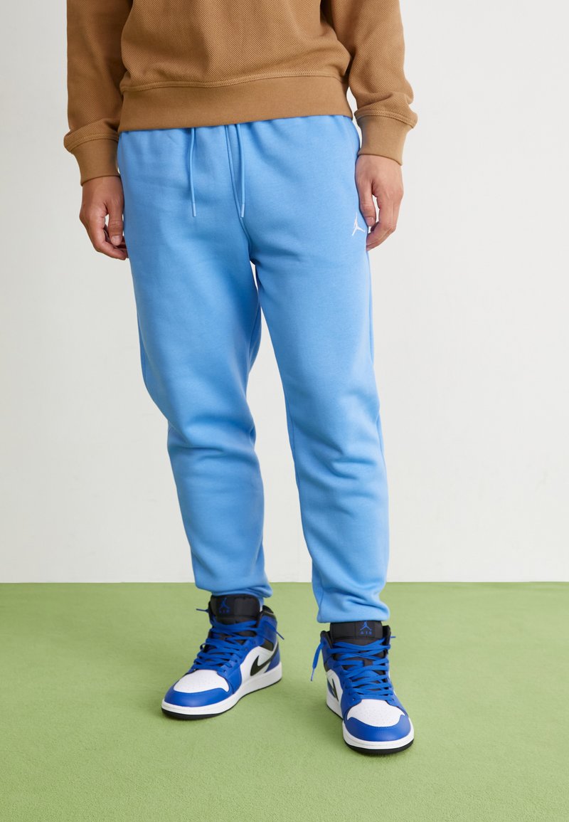 Lichtblauwe sweatpants met een elastische tailleband en trekkoord. G gedragen met zwart-blauwe hoge sneakers met witte accenten.