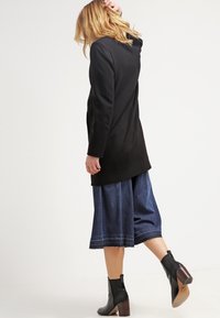 Mustapituinen pitkä takki, farkku culottes-housut ja mustat nilkkurit puukorkoilla. Pehmeä pinta, jossa on kontrastiväriset tikkaukset culottien helman läheisyydessä.