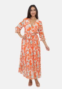 Maxi kjole i orange med blomstertryk, med en indpakningsdesign, lange ærmer med bindebånd og en plisseret nederdel. Klare åbne tå sandaler.
