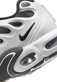 Białe i czarne sneakersy Nike z teksturowaną cholewką, wyraźnym falistym wzorem, widoczną poduszką powietrzną oraz czarnym logo Swoosh.