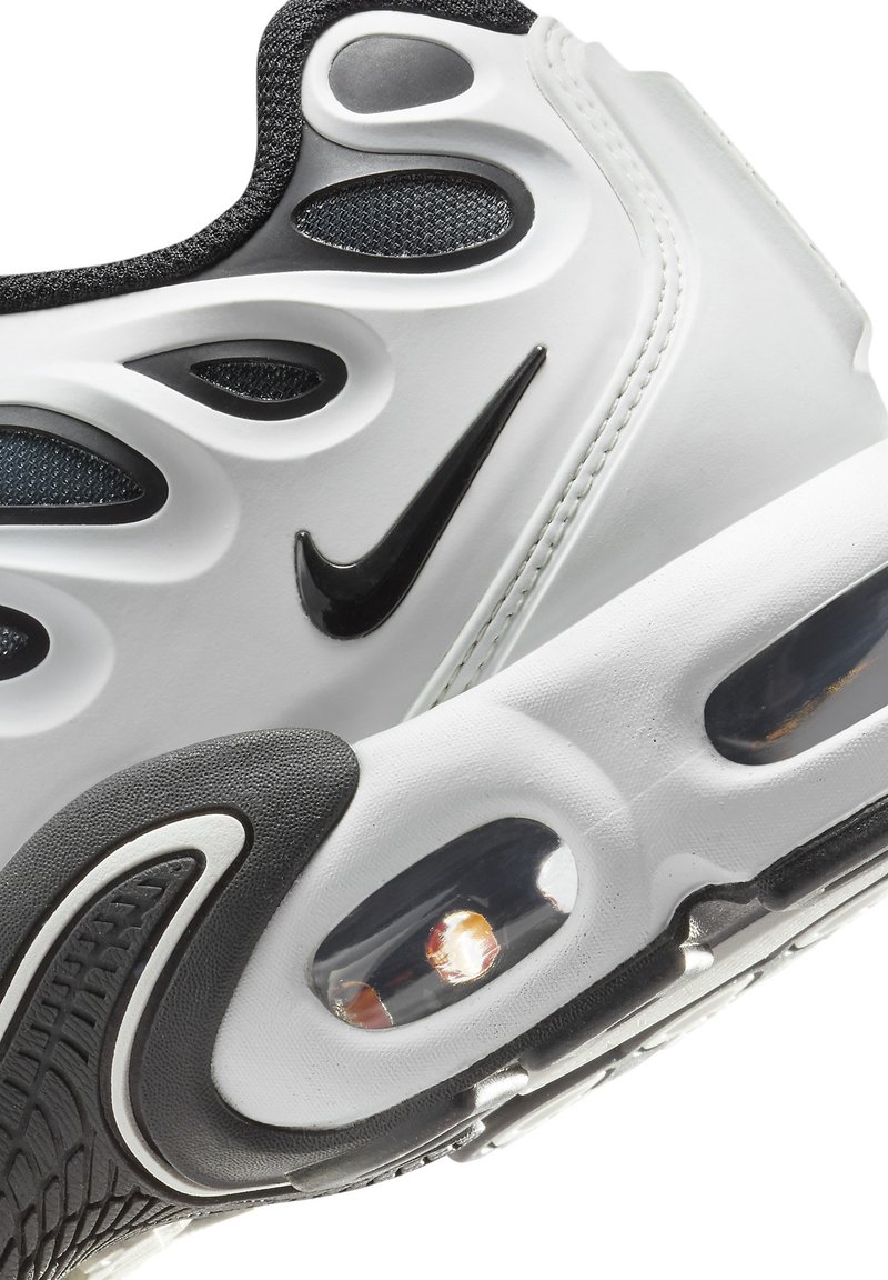 Baskets Nike blanches et noires avec une tige texturée, un design ondulé proéminent, un amorti visible et un logo swoosh noir.