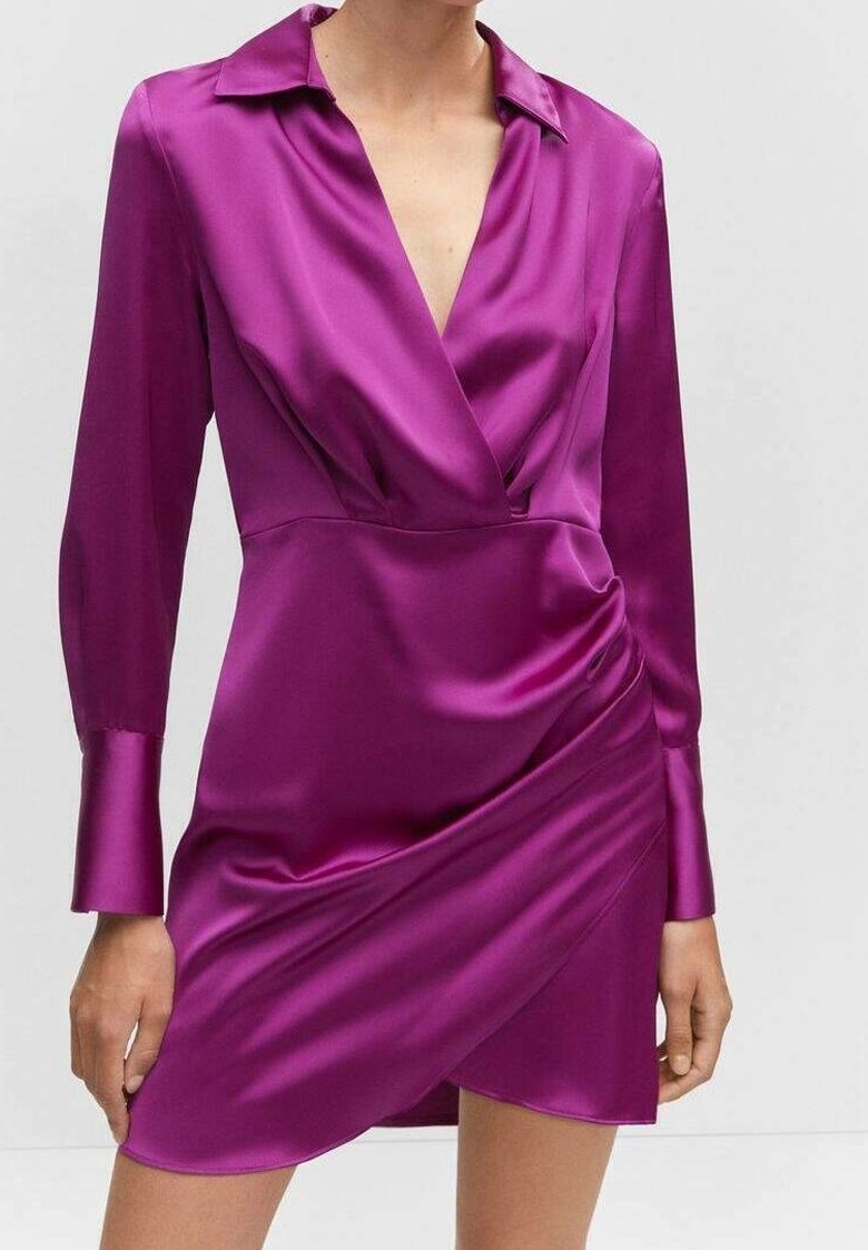 Frau in einem lilafarbenen Satin-Wickelkleid mit langen Ärmeln und tiefem V-Ausschnitt sowie Raffungen an der linken Hüfte.